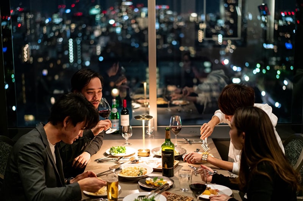 BALCON TOKYOの店内・夜景が見える窓際のダイニング席で食事を楽しむ様子