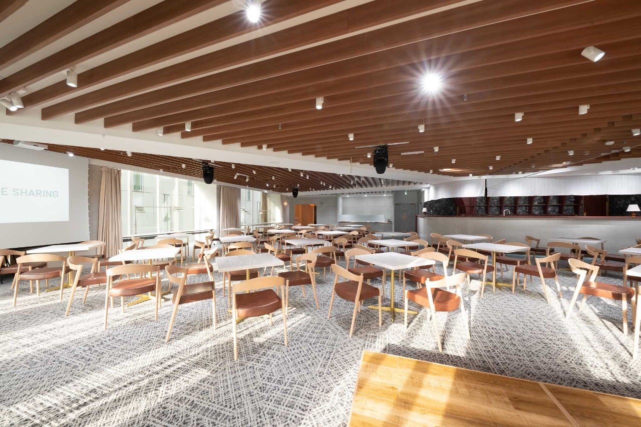 GLADE PARK 新宿駅前の宴会場内観。木ルーバー天井と大きな窓、大理石調テーブルと木製チェアの大型ホール