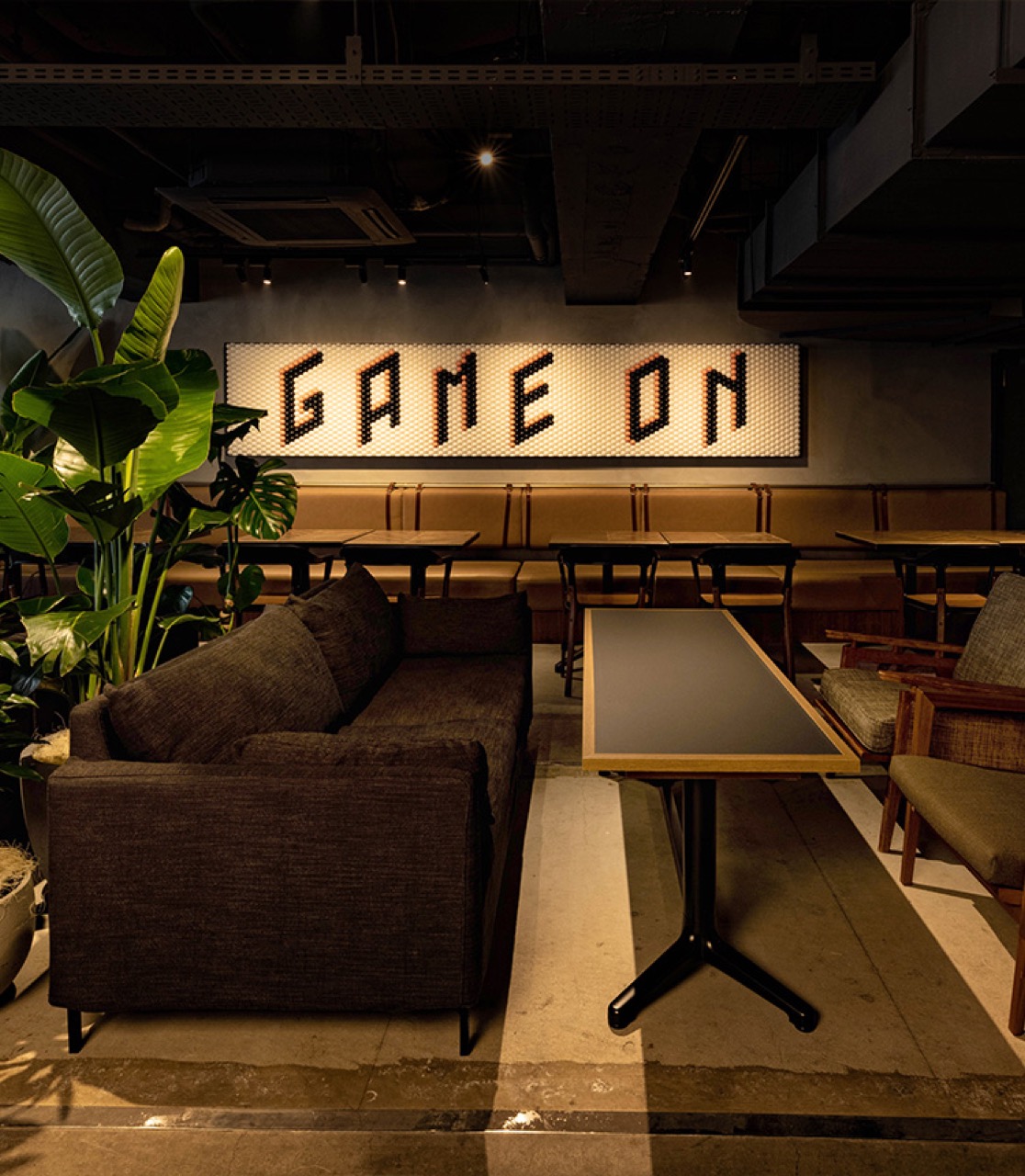 T4 KITCHEN 渋谷店の店内。ソファ席とテーブル席が並び、奥の壁に「GAME ON」のライトアートと観葉植物を配したカジュアルな貸切空間